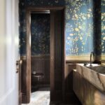 Modrá tapeta so zlatým kvetinovým vzorom, kamenné umývadlo a tmavé drevené obloženie v luxusnej kúpeľni.