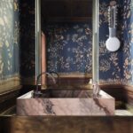 Masívne kamenné umývadlo, mosadzné detaily a modrá tapeta s prírodným motívom v nadčasovom dizajne.