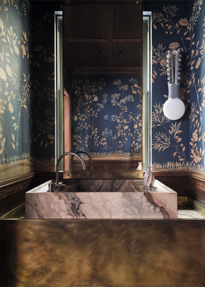 Masívne kamenné umývadlo, mosadzné detaily a modrá tapeta s prírodným motívom v nadčasovom dizajne.
