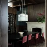 Jedáleň so skleneným lustrom nad čiernym stolom s vínovými stoličkami v tmavom drevenom interiéri.