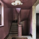 Schodisko s dreveným stupňami, zaobleným zábradlím a ružovými stenami i stropom.