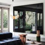 Obývacia izba s veľkou televíznou obrazovkou na stene za dizajnovou lampou a kamenným stolíkom na vzorovanom koberci.