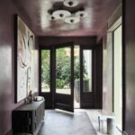 Chodba s fialovou stenou, abstraktným obrazom, nízkou skrinkou a presklenými dverami na terasu.