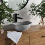 Sivé kamenné umývadlo v tvare misy, matná čierna batéria a masívna drevená skrinka s výraznou textúrou dreva.