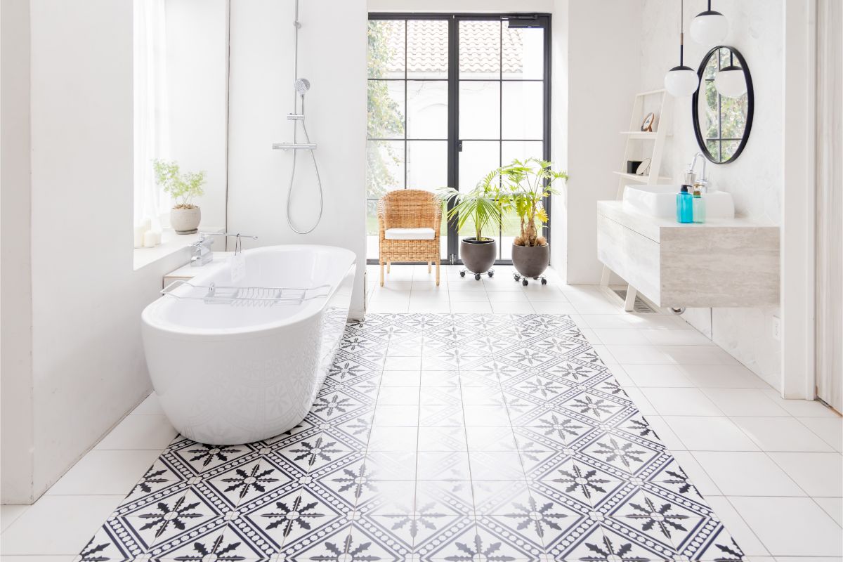 Presvetlený interiér s výraznou vzorovanou dlažbou, bielou vaňou, čiernymi kovovými dverami a živými zelenými rastlinami.