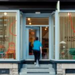 Svetlomodrý vstup do budovy s veľkými výkladmi, červenými kresbami a tehlovým soklom.