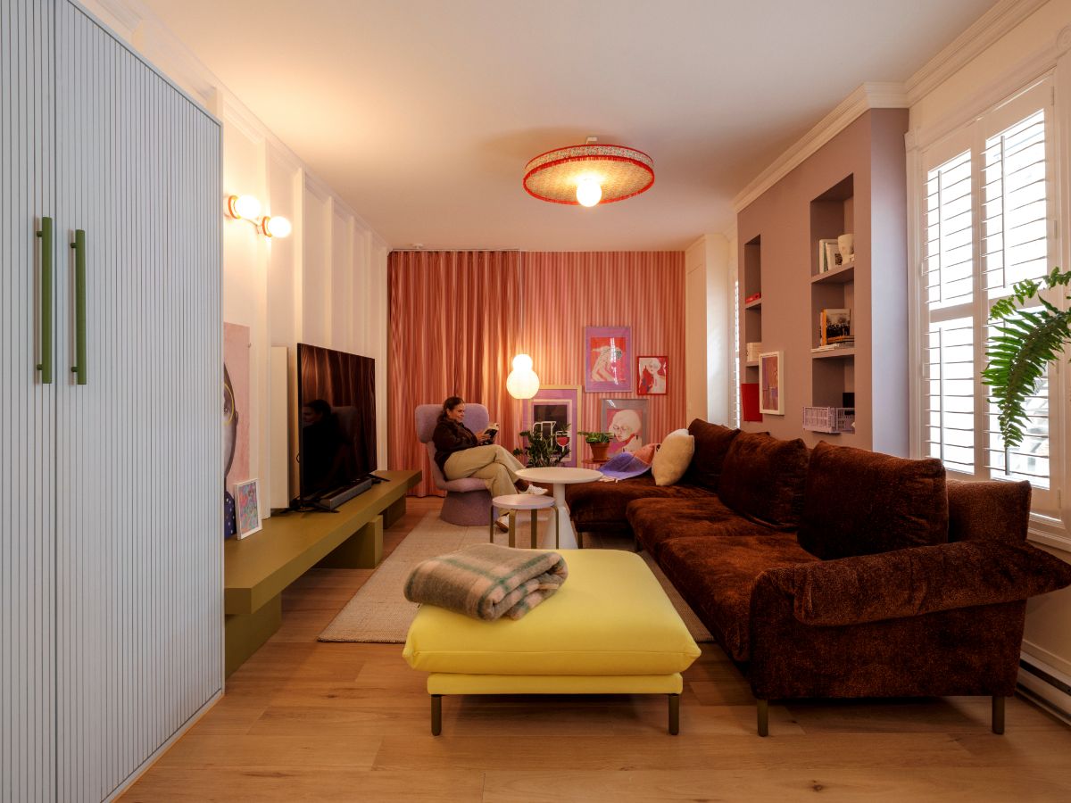 Moderná obývacia izba s hnedou zamatovou sedačkou, žltou taburetkou, ružovými závesmi a drevenou podlahou.