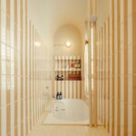 Úzka biela vaňa v kúpeľni s vertikálnym béžovým obkladom a oblúkovým stropom.