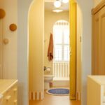 Kúpeľňový priestor s béžovou podlahou, žltou harmonikovou stenou a bielym oblúkom vedúcim k toalete.