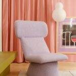 Fialové vlnené kreslo na sivom koberci pred červeným pruhovaným závesom s bielym guľatým svietidlom.