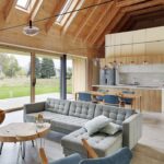 Presvetlená otvorená obývacia izba s dreveným krovom, sivou modulárnou sedačkou a výhľadom cez veľkoformátové okná do záhrady.