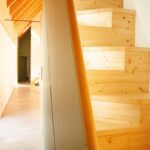 Interiérové schodisko zo svetlého dreva s oblým zábradlím vedúce do podkrovia pod šikmú strechu s dreveným obkladom.