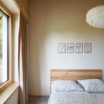 Svetlá spálňa s drevenou posteľou, kvetovanými obliečkami, jemnými béžovými závesmi a sériou štyroch botanických obrazov.