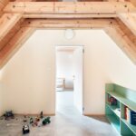 Detská herňa v podkroví s dreveným krovom, svetlou podlahou, mätovými policami a rozloženými farebnými hračkami.