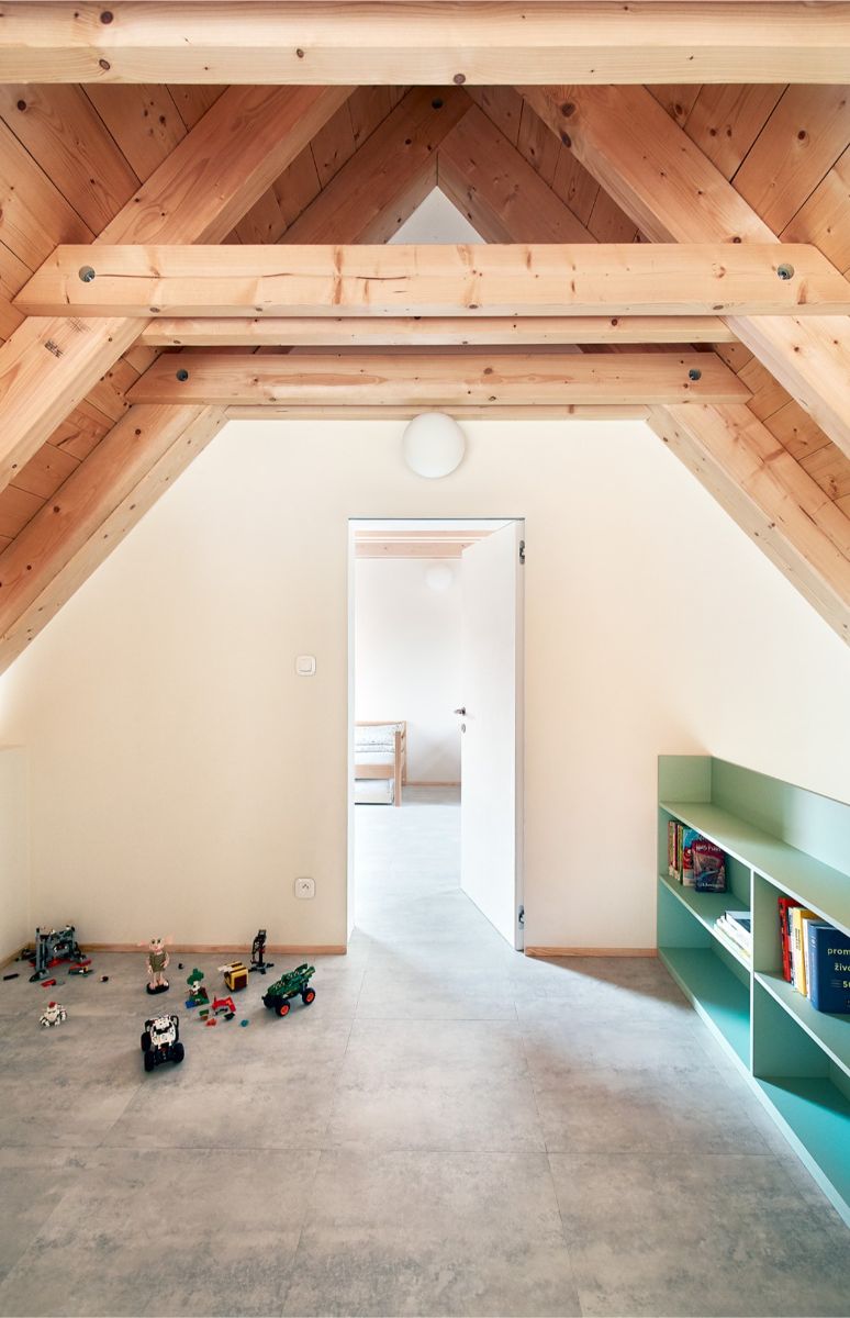 Detská herňa v podkroví s dreveným krovom, svetlou podlahou, mätovými policami a rozloženými farebnými hračkami.