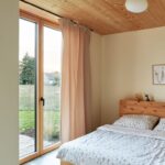 Presvetlená spálňa s dreveným nábytkom, veľkým francúzskym oknom do záhrady a priznaným dreveným podhľadom.