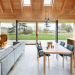 Jedálenský kút s masívnym dreveným stolom, modrými čalúnenými stoličkami a dizajnovými sklenenými svietidlami pod šikmým stropom.