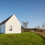 Moderná biela novostavba s červenou šikmou strechou a veľkoformátovými oknami v rozľahlej zatrávnenej záhrade.