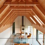 Vysoký otvorený priestor s drevenou konštrukciou krovu, visiacimi čiernymi káblami so svietidlami a jedálenským sedením.