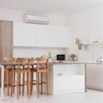 Moderná kuchynská linka v bielom a drevenom dizajne s bielymi skrinkami a kuchynským ostrovčekom s barovým sedením.