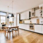 Kuchyňa s bielou kuchynskou linkou pozdĺž steny a dreveným jedálenským stolom.