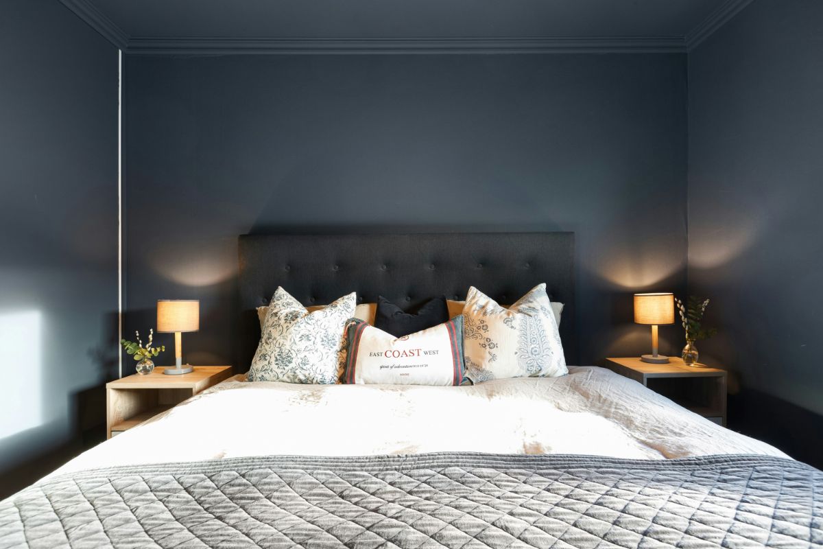 Spálňa s tmavými stenami aj stropom a s posteľou s čiernym čalúneným čelom.