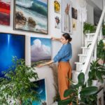 Žena vešajúca obraz ma stenu k ostatným obrazom nad schodisko.