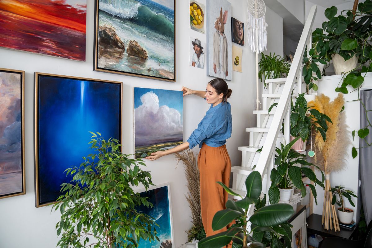 Žena vešajúca obraz ma stenu k ostatným obrazom nad schodisko.