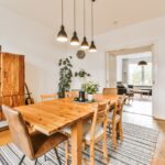 Masívny drevený stôl pod modernými čiernymi lampami na pruhovanom tkanom koberci v presvetlenom interiéri.