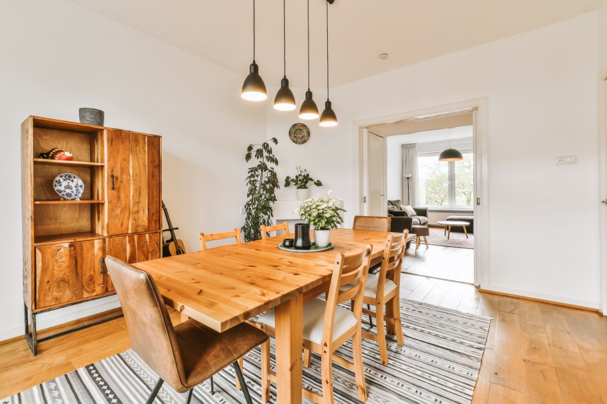 Masívny drevený stôl pod modernými čiernymi lampami na pruhovanom tkanom koberci v presvetlenom interiéri.