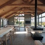 Otvorený interiér s priznaným krovom, moderným čiernym krbom, svetlou kuchyňou a veľkoformátovým presklením.