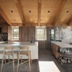 Kuchynský ostrov s bielym lamelovým čelom, orechovými skrinkami, drevenými trámami a umeleckou tapetou s palmami.