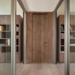 Minimalistická chodba s vysokými orechovými knižnicami, drevenými dverami bez zárubne a presklenými bočnými stenami.