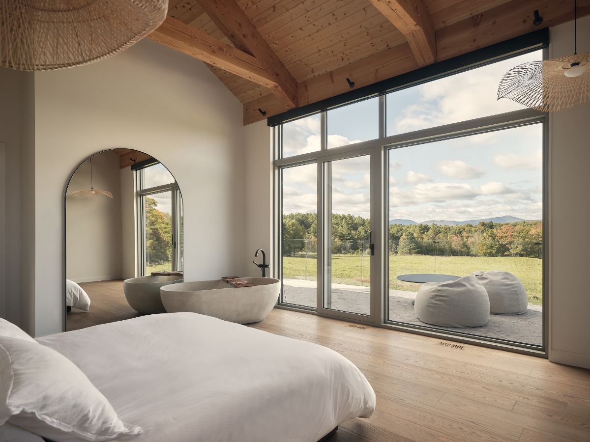 Svetlá spálňa s voľne stojacou kamennou vaňou, dreveným trámovým stropom a veľkoformátovým presklením do prírody.