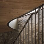 Vnútorné schodisko s kovovým zábradlím pri stene z prírodného kameňa pod dreveným obkladom stropu.