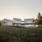 Moderné vidiecke sídlo s kaskádovitou architektúrou, svetlým dreveným obkladom a veľkoformátovými oknami na trávnatom svahu.