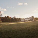 Panoráma moderného sídla so šedou strechou a kamennou fasádou v otvorenej krajine s jesennými stromami a lúkou.