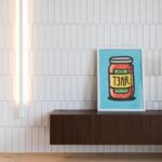 Modrý rámovaný obraz na tmavej drevenej skrinke pred bielym lesklým obkladom a svetlou podlahou.