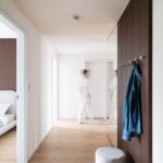 Vstupná hala s vešiakovou stenou na tmavom lamelovom paneli vedľa sivého taburetu.