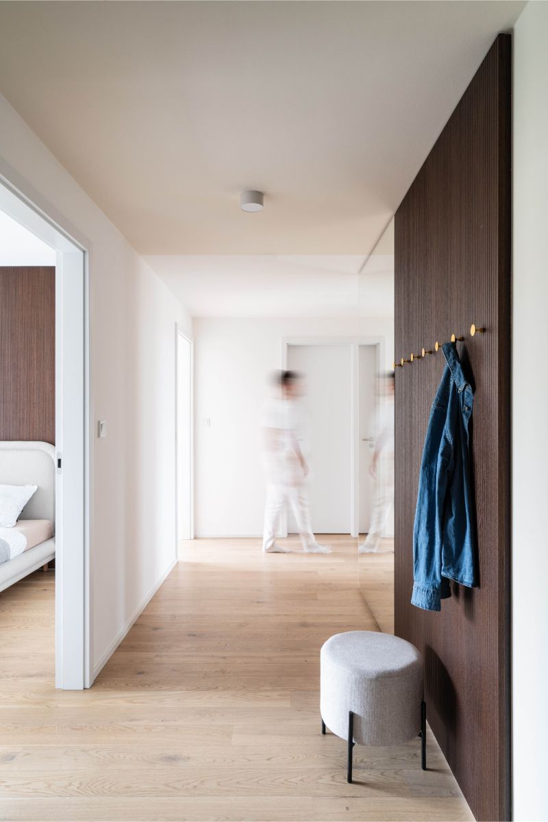 Vstupná hala s vešiakovou stenou na tmavom lamelovom paneli vedľa sivého taburetu.