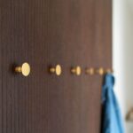 Detail na stenu s tmavým dreveným obložením a zlatými vešiakmi.