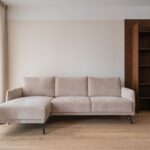 Béžová rohová sedačka na dubových parketách vedľa tmavohnedej vstavanej knižnice v minimalistickej obývačke.