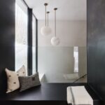 Čierne relaxačné zákutie s vankúšmi, sklenené zábradlie a tri biele guľové lampy visiace zo svetlého stropu.