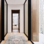 Svetlá chodba s drevenými lamelami, vzorovaným kobercom a presklenými stenami smerujúcimi do zimnej krajiny.