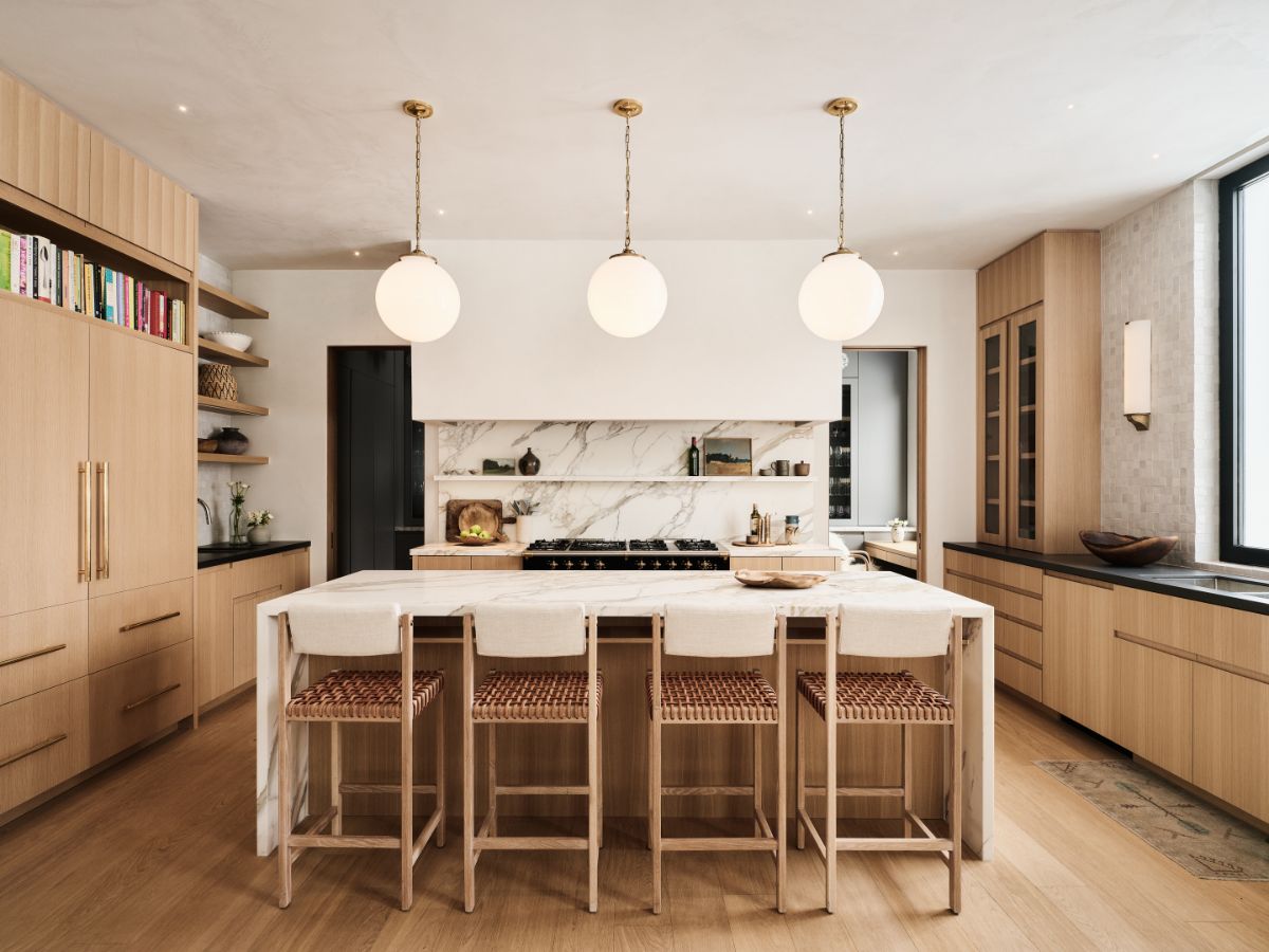 Kuchyňa s dreveným ostrovom, mramorovou pracovnou doskou, bielymi guľovými lampami a prútenými barovými stoličkami.