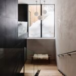 Drevené schodisko s tmavým obkladom steny, visiacimi svietidlami a okienkom na zasnežený exteriér horskej chaty.