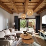 Svetlá obývacia izba s dreveným trámovým stropom, béžovou rohovou sedačkou a dvoma prútenými lustrami.