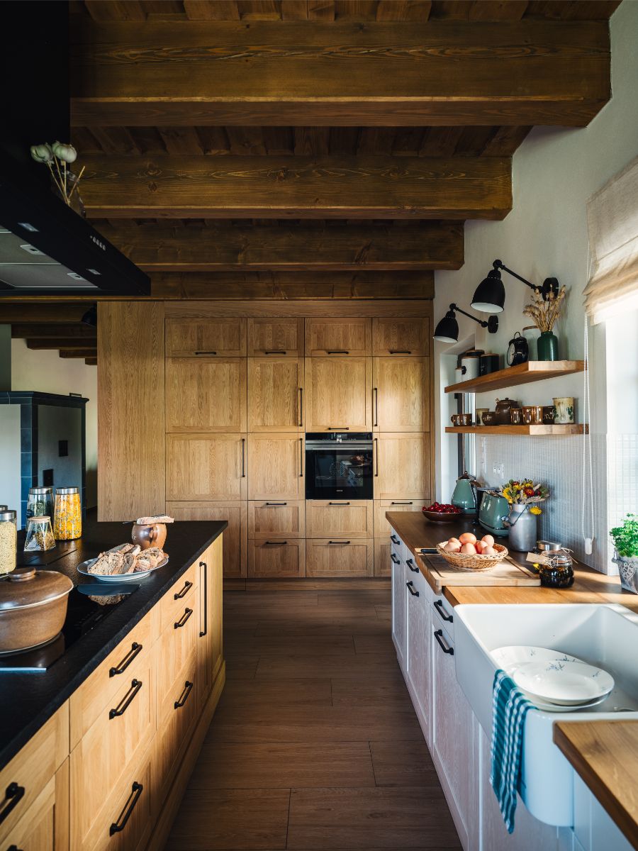 Kuchyňa s drevenou doskou, bielym keramickým drezom a čiernou batériou pred oknom.