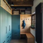 Modrá šatníková zostava s čiernymi úchytkami a drevený výklenok s vešiakmi a lavičkou v modernej predsieni.