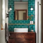 Biely keramický drez na tmavej drevenej skrinke pred stenou so sýtozeleným obkladom a obdĺžnikovým zrkadlom.